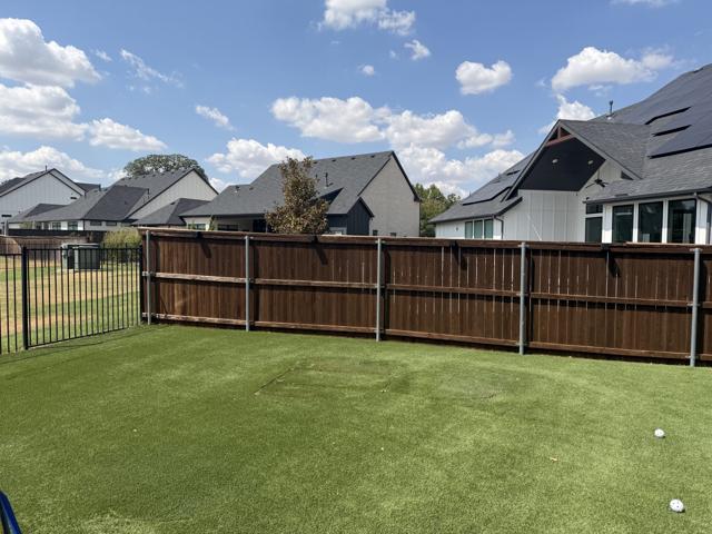 The same fenced backyard after removal, an empty stretch of artificial turf with only faint marks where the playset stood