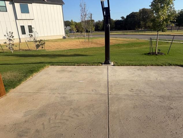 The same driveway swept clean after the haul-off, with nothing left but bare concrete and the lawn beyond