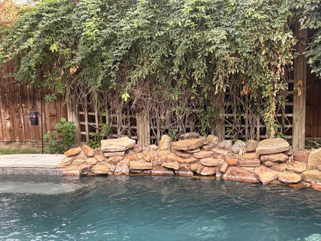 Dense overgrown vines covering a weathered wooden lattice trellis behind the rock border of a backyard pool